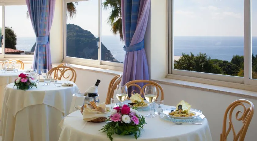 Sala ristorante con tavoli apparecchiati e ampie finestre sul mare